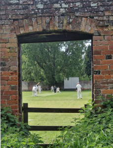 Erlestoke Cricket Club playing cricket through an old brick window frame.
